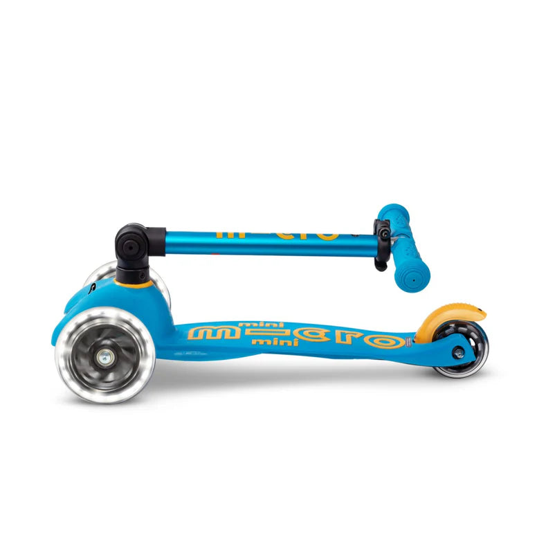 Micro Mini Deluxe Foldable LED Scooter, blue with orange decals, folded with stem tucked for compact storage.