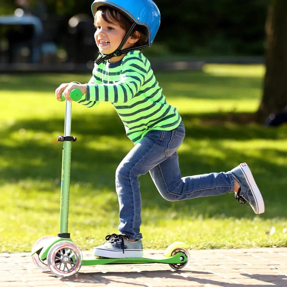 Micro Mini Deluxe Scooter in lime green; child in blue helmet rides outdoors, showing balance and motion.