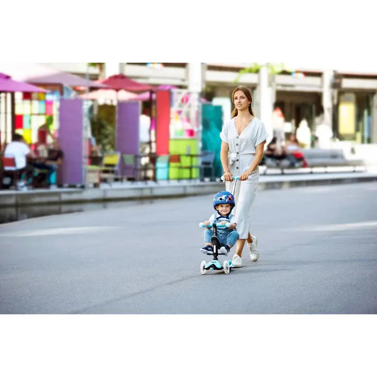 Micro Mini2Grow Deluxe LED Scooter; toddler in helmet rides as a woman guides him along a sunny outdoor plaza.