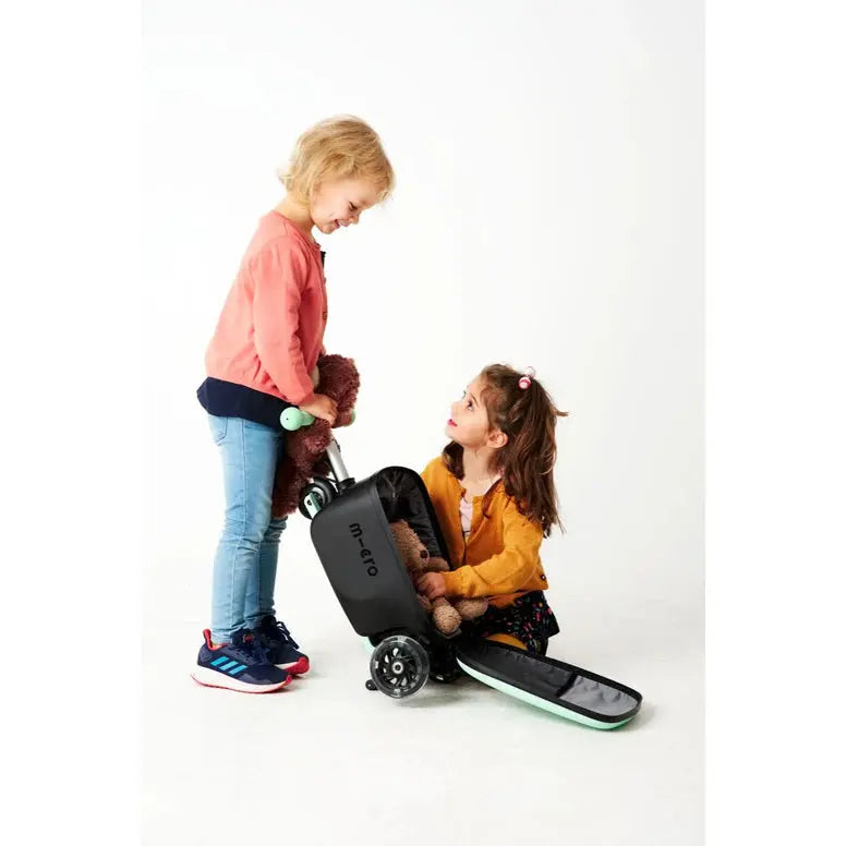 Micro Scooter Junior Luggage Mint; mint-colored kid's luggage scooter as a child loads a teddy into the storage compartment.