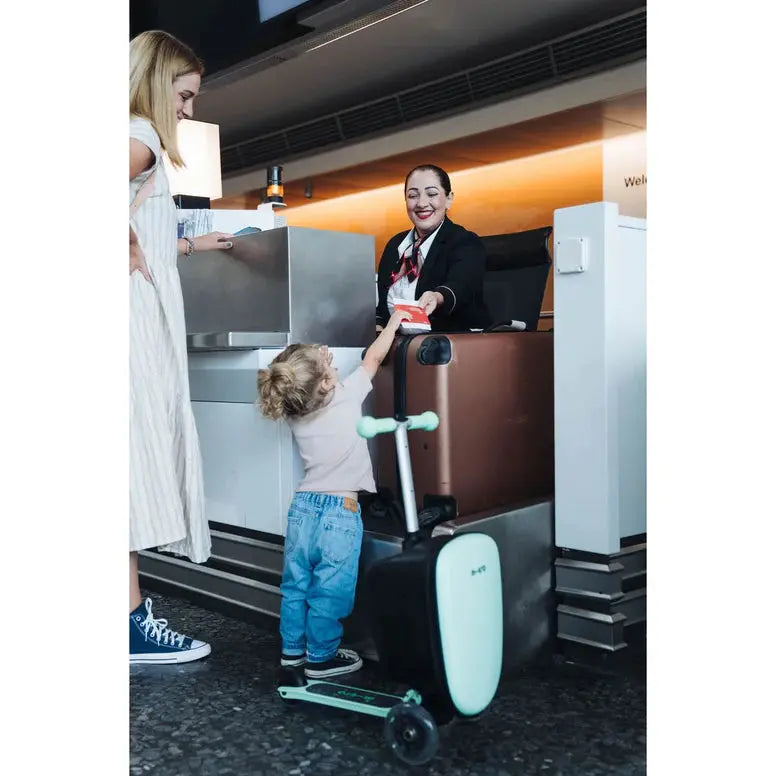 Micro Scooter Junior Luggage Mint kid-friendly suitcase with built-in scooter; child hands passport to an airline attendant at check-in.