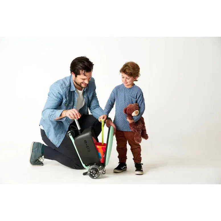Micro Scooter Junior Luggage Mint luggage cart in mint frame, parent kneels guiding it beside a child holding a teddy.