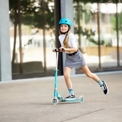 Micro Sprite LED Scooter ridden by a girl gliding outdoors on a teal frame with a white deck, blue helmet.