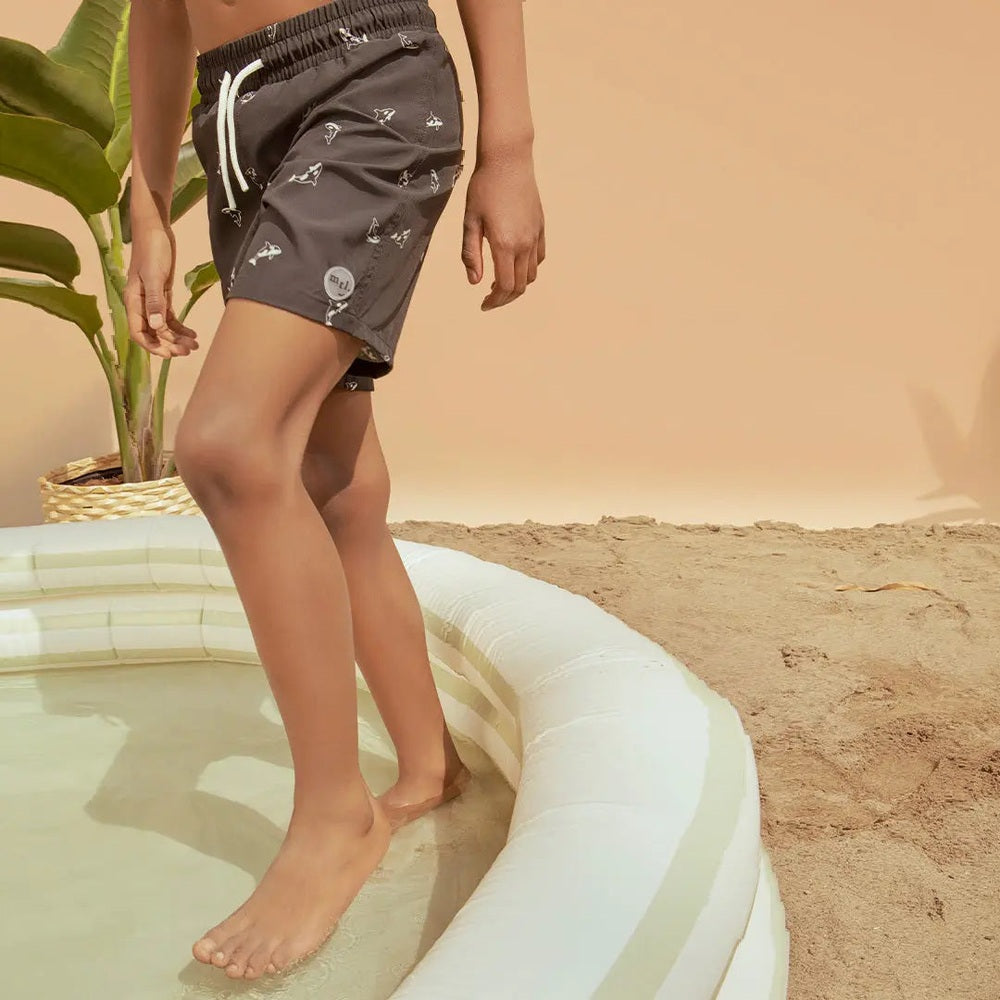 Miles The Label Orca Print Swim Trunks in black with white drawstring, shown being worn by a model standing at the pool edge.