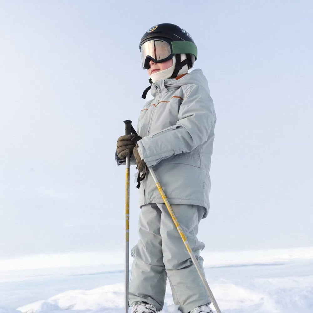 Mini A Ture Matadane Ski Tech Jacket Grs Quarry worn by a skier in a light grey jacket gripping ski poles in a snowy scene