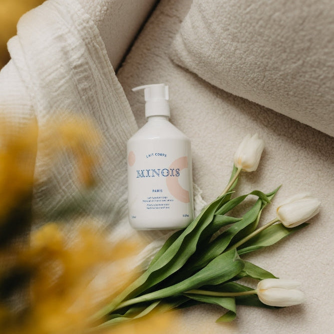 Minois Paris body lotion bottle with pump on beige towel beside white tulips