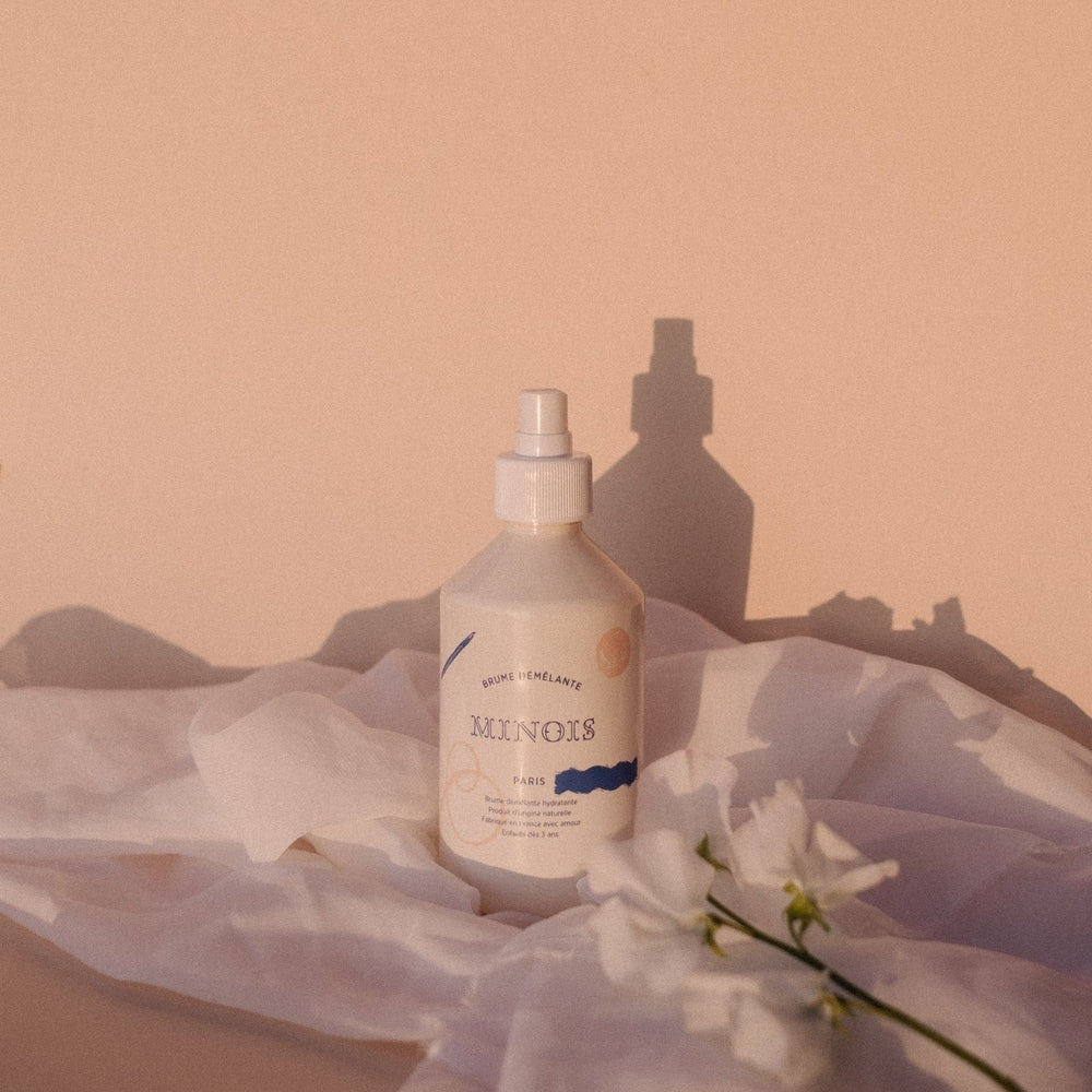 Minois Paris Detangling Mist 300 ml bottle, white plastic with spray, set against peach backdrop.