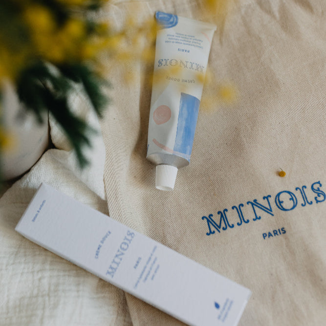 Minois Paris face and body cream tube in white/blue packaging on beige fabric