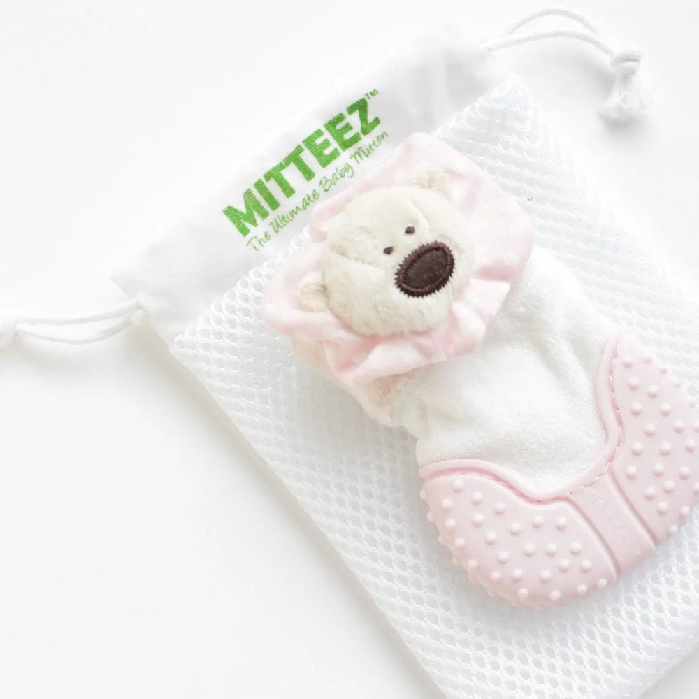 MITTEEZ Organic Developmental Teething Mitten in white with pink silicone palm texture and plush bear charm, shown with mesh bag