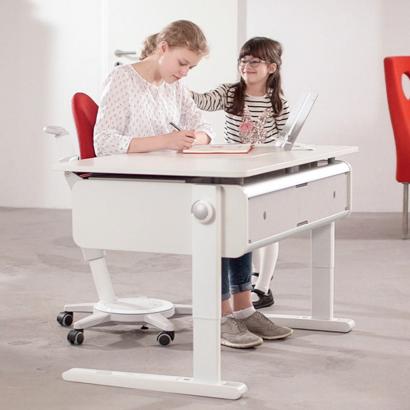 MOLL Champion Height Adjustable Desk Left Up, white with storage drawer; two kids study together while one writes.