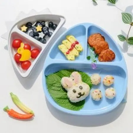 Monee Dinosaur Food Plate Combo blue divided plate with bunny rice, greens, croquettes; white tray holds blueberries and tomatoes