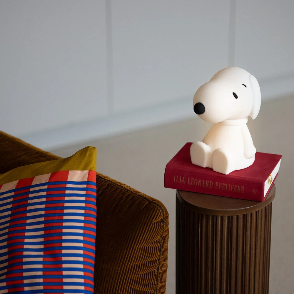 MR MARIA Bundle of Light Snoopy figurine, white dog perched on red book atop brown pedestal beside striped cushion