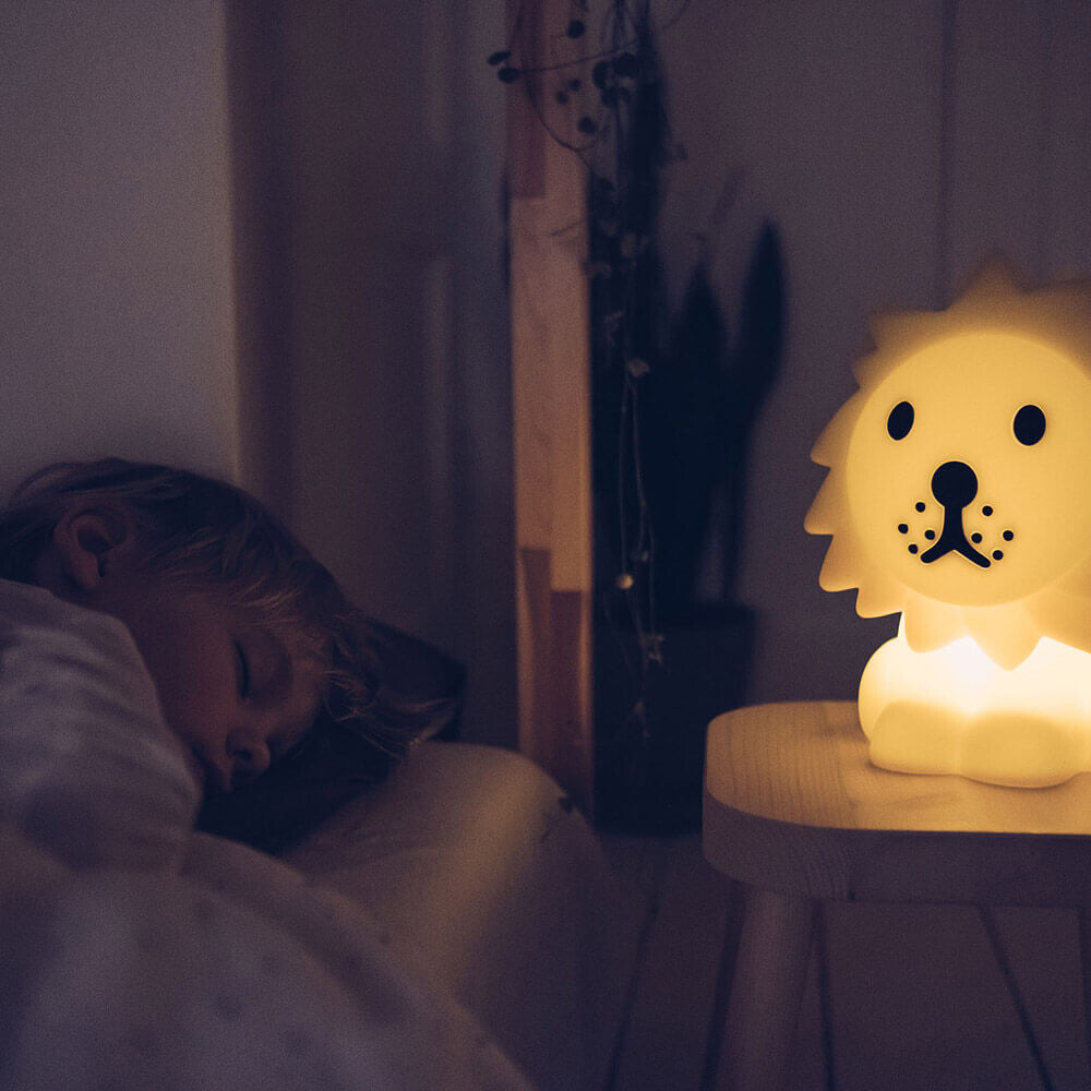 Mr Maria First Light Lion night light with warm yellow glow on bedside table beside sleeping child