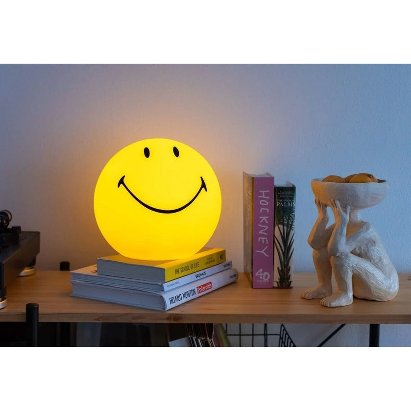 MR MARIA Star Light Smiley lamp, yellow ambient glow on a bookshelf with books and decor.