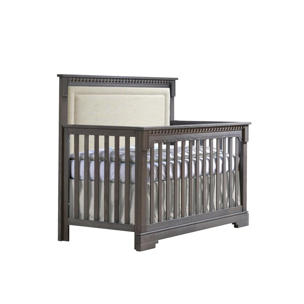 Natart Ithaca 5-in-1 Convertible Crib with beige upholstered headboard in dark wood finish, sturdy slat sides