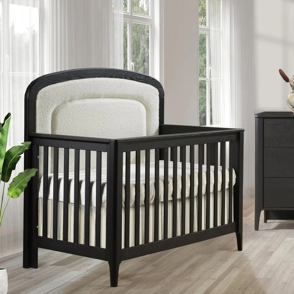 Natart Palo 5-in-1 convertible crib in black wood with cream upholstered headboard panel.