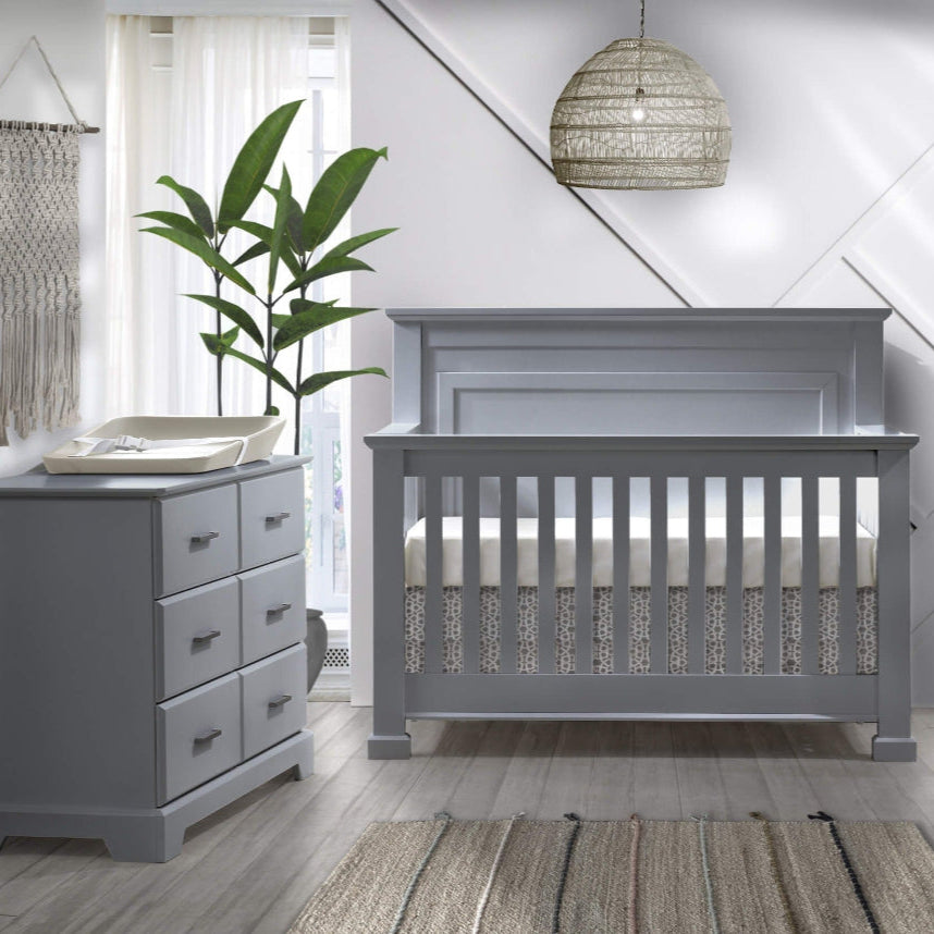 Natart Taylor 5-Drawer Dresser in gray beside a matching crib in a bright modern nursery.