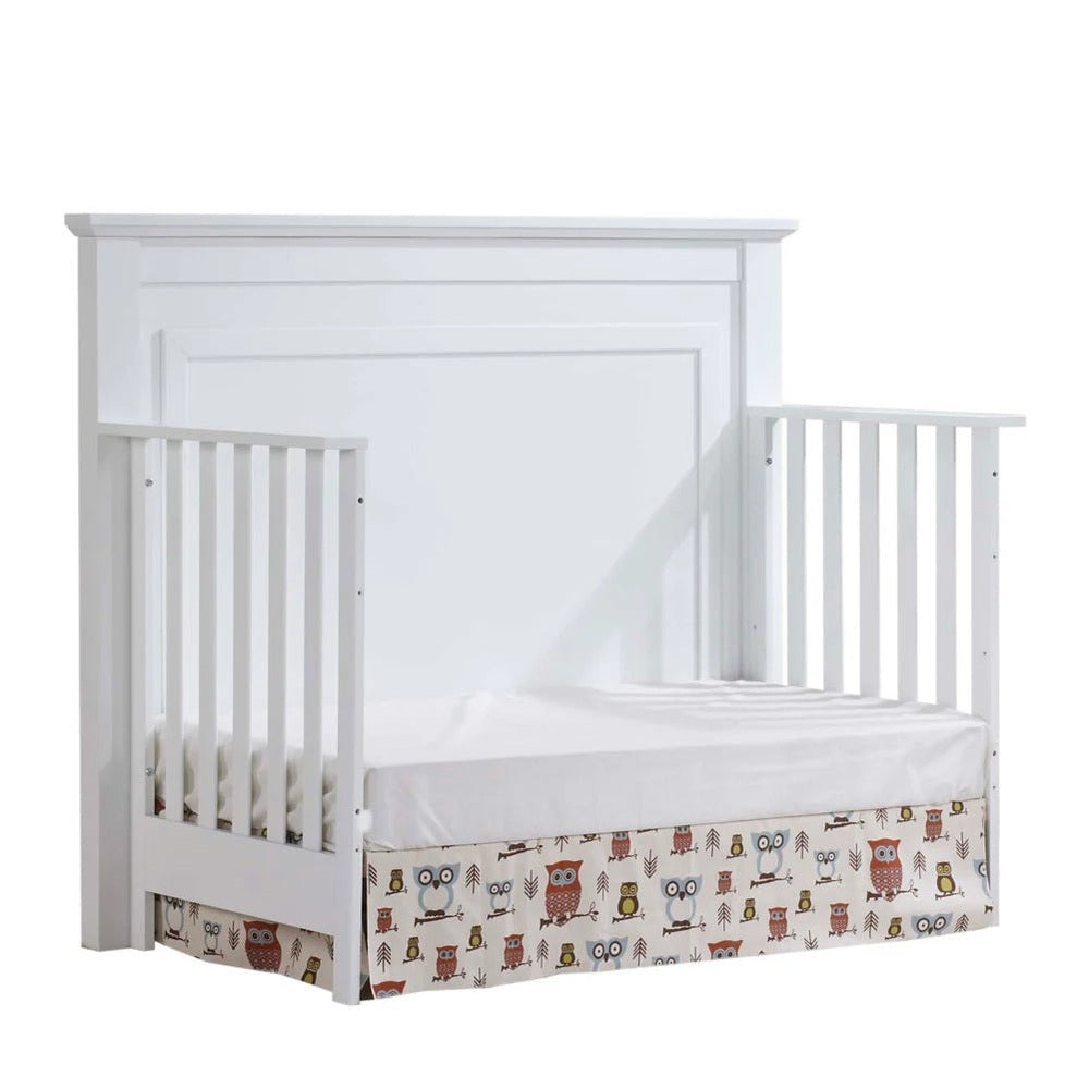 Natart Taylor 5-in-1 convertible crib in white with slatted sides and an owl-print fabric skirt