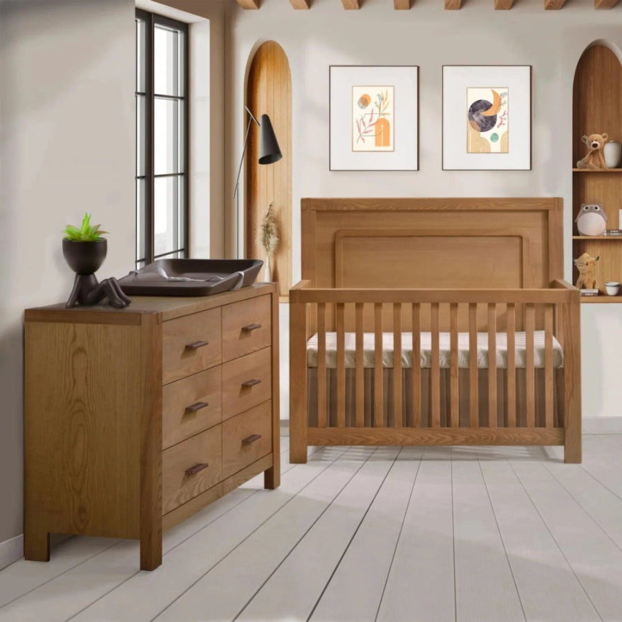Natart Signature Series Toscano 57 Inch Double Dresser in oak with a changing tray atop in a cozy nursery scene.
