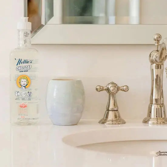 Nellie's One Soap 570 ml bottle with pump sits on a bathroom sink beside a blue ceramic cup and chrome faucet.