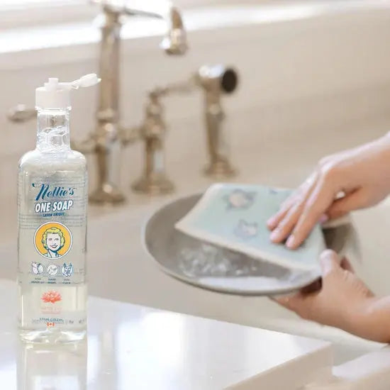Nellie's One Soap 570 ml bottle with pump, translucent soap, sits by the sink as hands wash a dish.