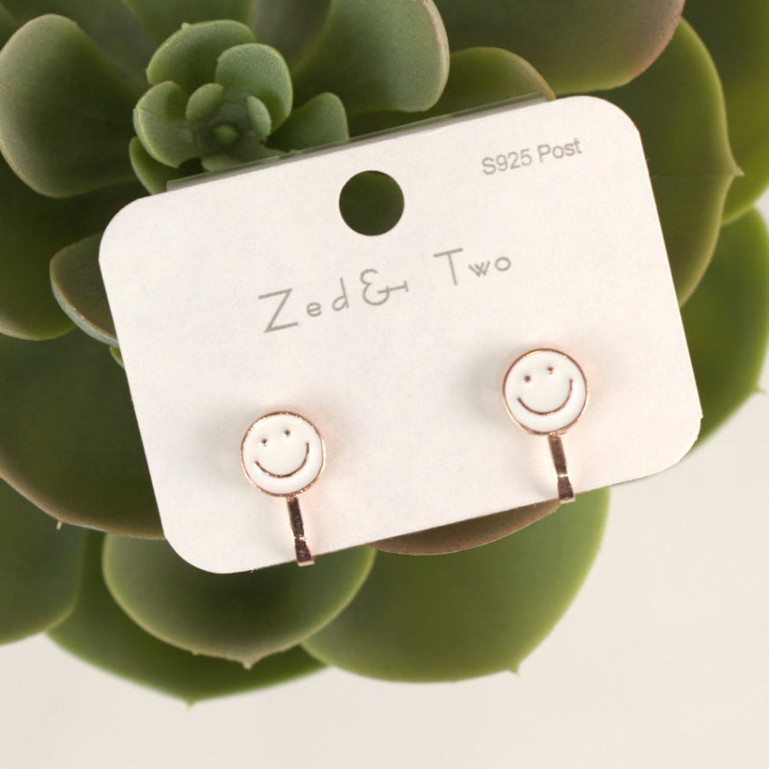 Nemibaby Smile Earrings pair on display card, white enamel faces with rose-gold posts