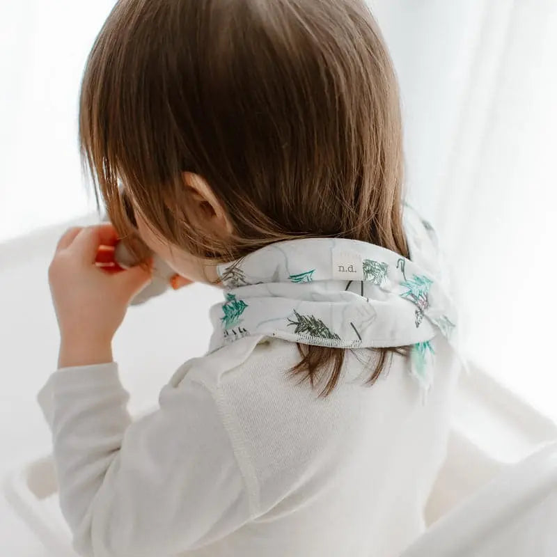 Nest Designs Bamboo Baby Bandana Bib One Size (3M-24M) on a toddler, white with teal palm tree print, gently wrapped around