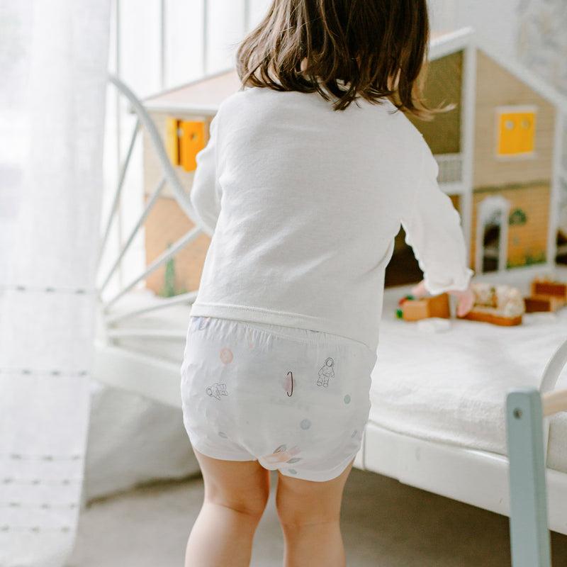 Nest Designs Bamboo Girls Boy Short Underwear 2-pack in white with pastel prints, as a child plays with a dollhouse.