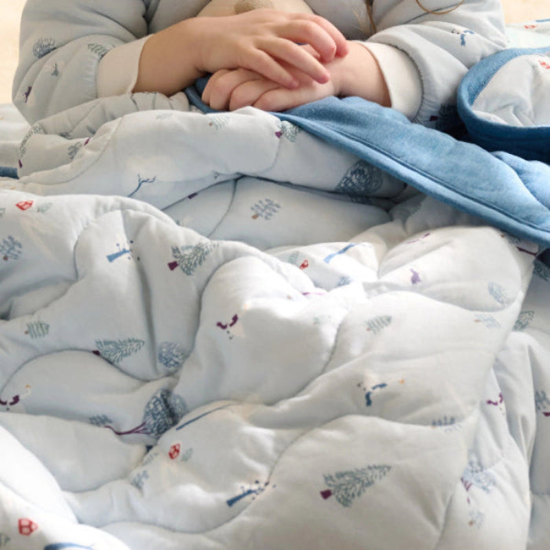 Nest Designs Bamboo Jersey Cozy Blanket Medium Snowy Snuggles, light blue quilt envelops a child with folded hands.