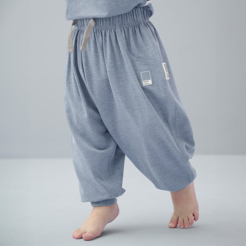 Nest Designs Bamboo Jersey Harem Pants Troposphere for babies, blue pants with elastic waist and beige drawstrings, shown walking barefoot.