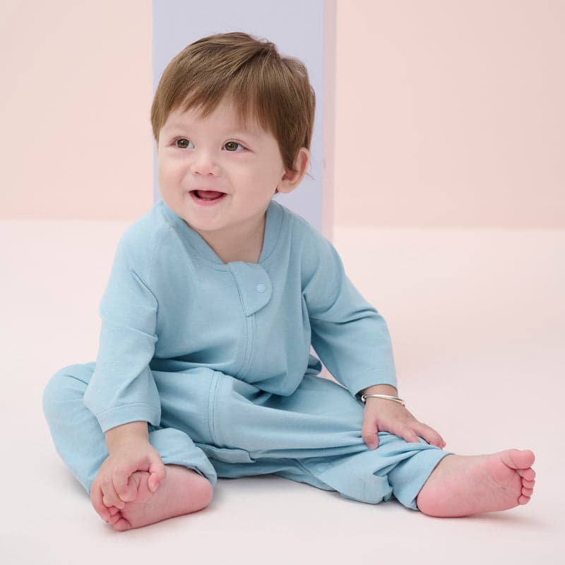 Nest Designs Bamboo Jersey Short Sleeve Footed Sleep Bag Forget-Me-Not, 0.6 Tog, baby sits smiling in pale blue sleepwear.