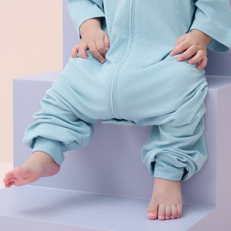 Nest Designs bamboo jersey short-sleeve footed sleep bag Forget-Me-Not blue, baby sits on pastel steps in 0.6 Tog sleepwear.