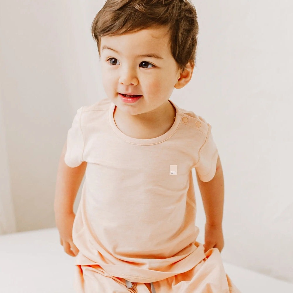 Nest Designs bamboo jersey short-sleeve T-shirt Pantone Bellini on a smiling toddler in peach color.