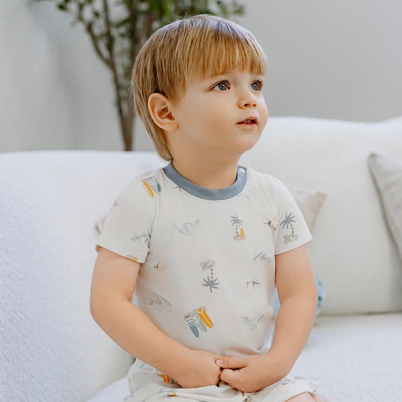 Nest Designs Bamboo Jersey Two-Piece Short Sleeve PJ Set Pastel Waves; toddler sits on couch in soft-print sleepwear