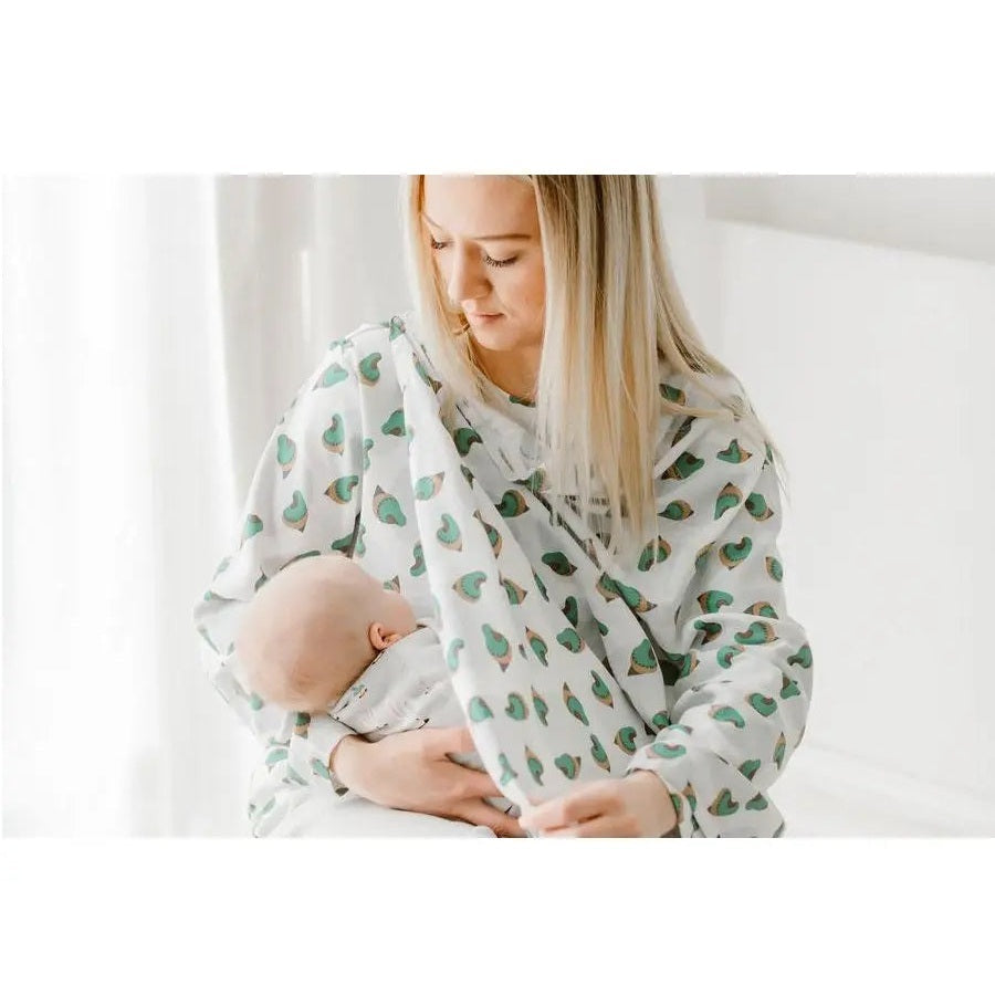 Nest Designs Bamboo Nursing Cover in white with green avocado print, worn by mother while nursing her baby.