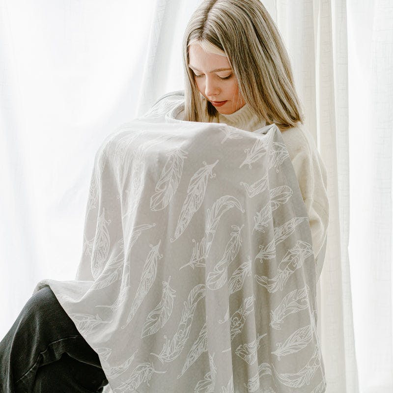 Nest Designs Bamboo Nursing Cover in beige with white feather print worn over the shoulders for discreet nursing.