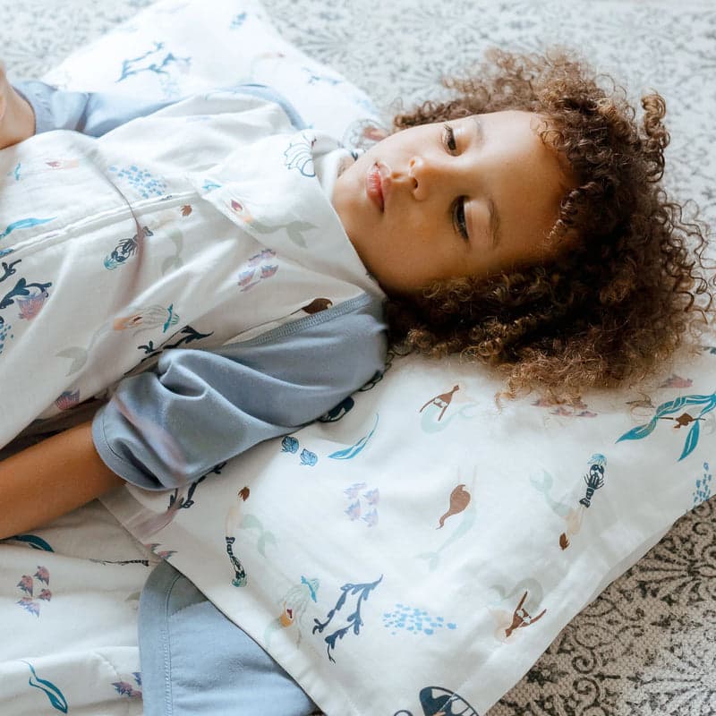 Nest Designs Bamboo Silk Toddler Pillow And Pillowcase Splish Splash set; child relaxing on blue sea-print bedding.