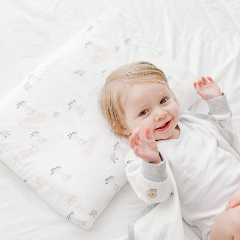 Nest Designs Bamboo Toddler Pillowcase Baby Baobabs pattern, toddler smiling on white bedding.