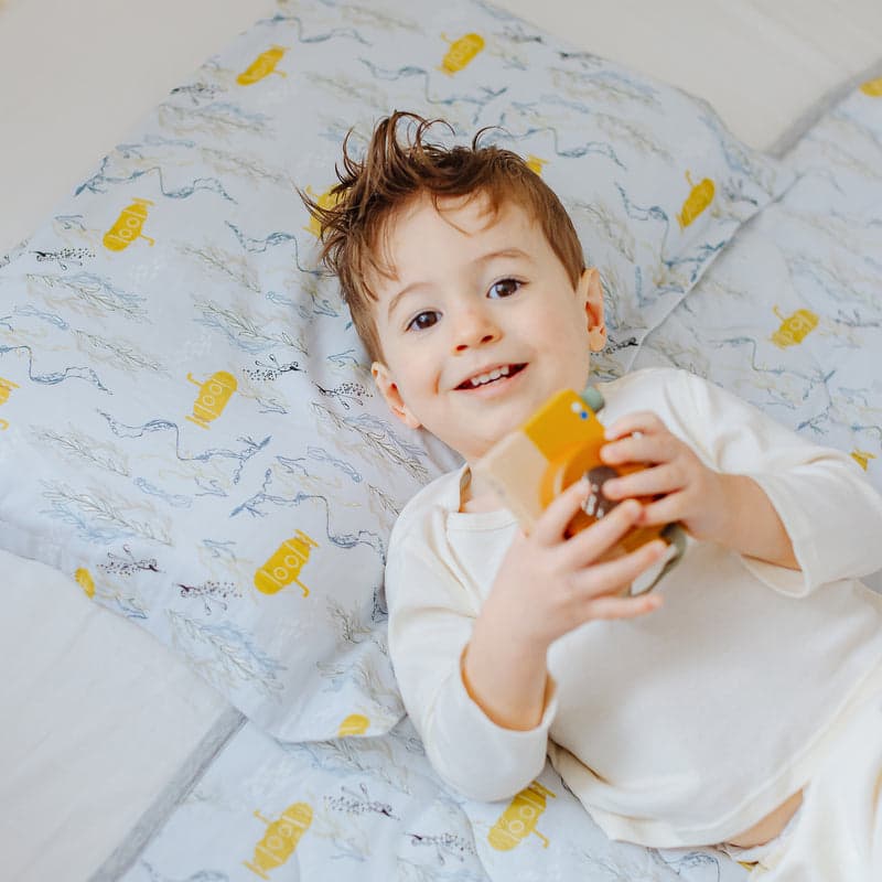 Nest Designs Bamboo Toddler Pillowcase Blub Blub Yellow Sub featuring yellow submarine print on light bedding with smiling child.