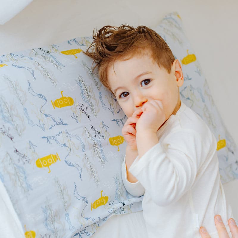 Nest Designs bamboo toddler pillowcase Blub Blub Yellow Sub, a child leans against a pillow covered in yellow submarines.