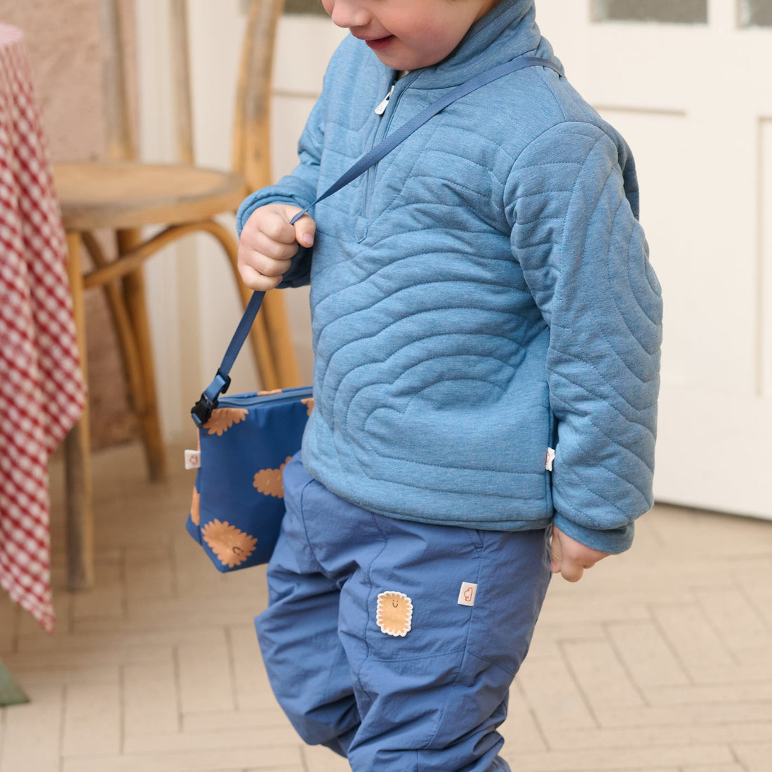 Nest Designs Biscuits and Vine waterproof bag in Biscuit Banter navy carried by its strap while a child walks indoors