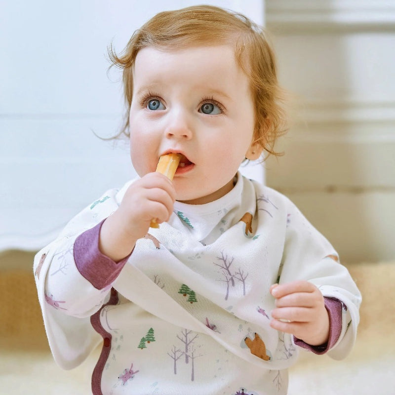 Nest Designs Burp'N Bib (2 Pack), white bib with woodland prints, worn by a baby chewing a cracker.
