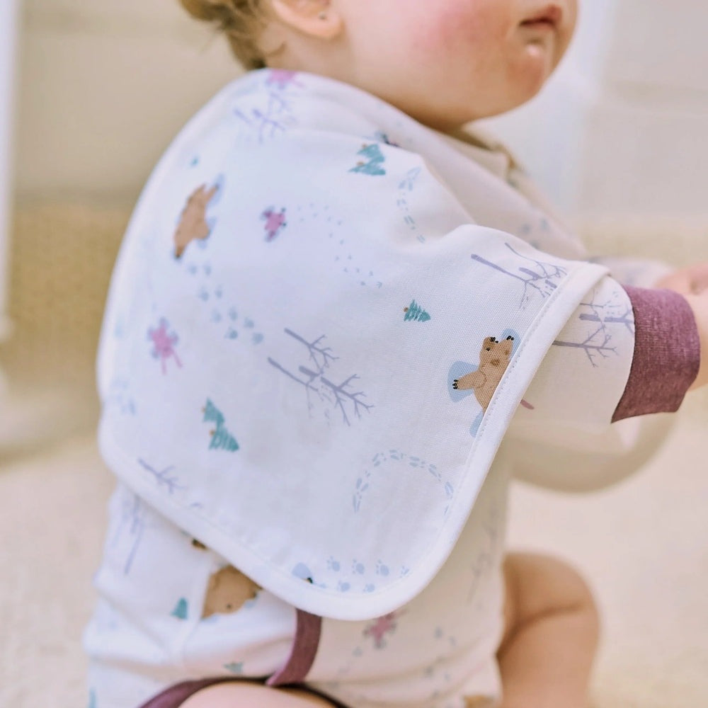 Nest Designs Burp'N Bib (2 Pack) white bib with bear and pine tree pattern being worn over the shoulder.