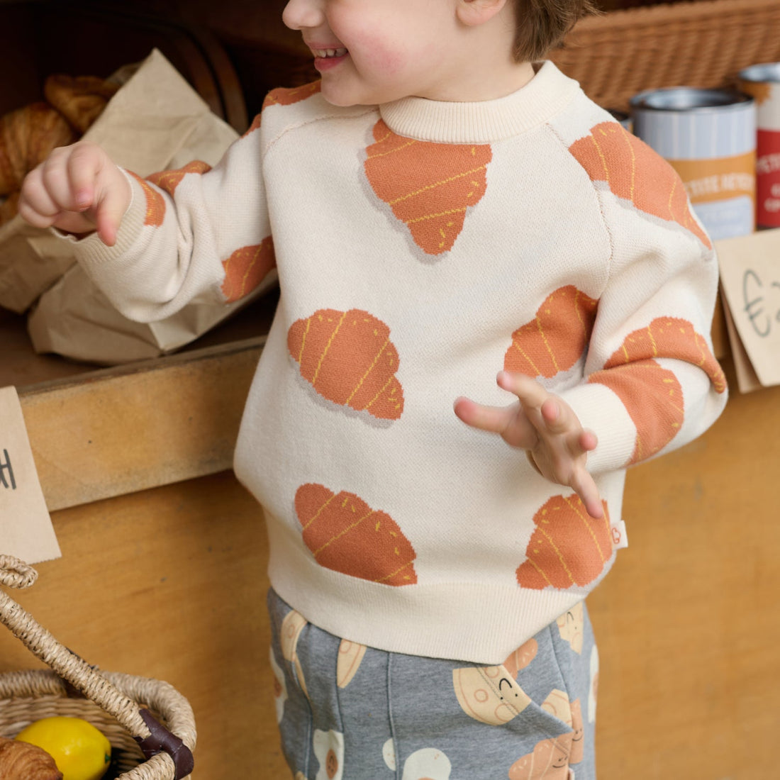 Nest Designs Cozy Croissants cream knit sweater, worn market close-up showing motifs across torso and sleeves