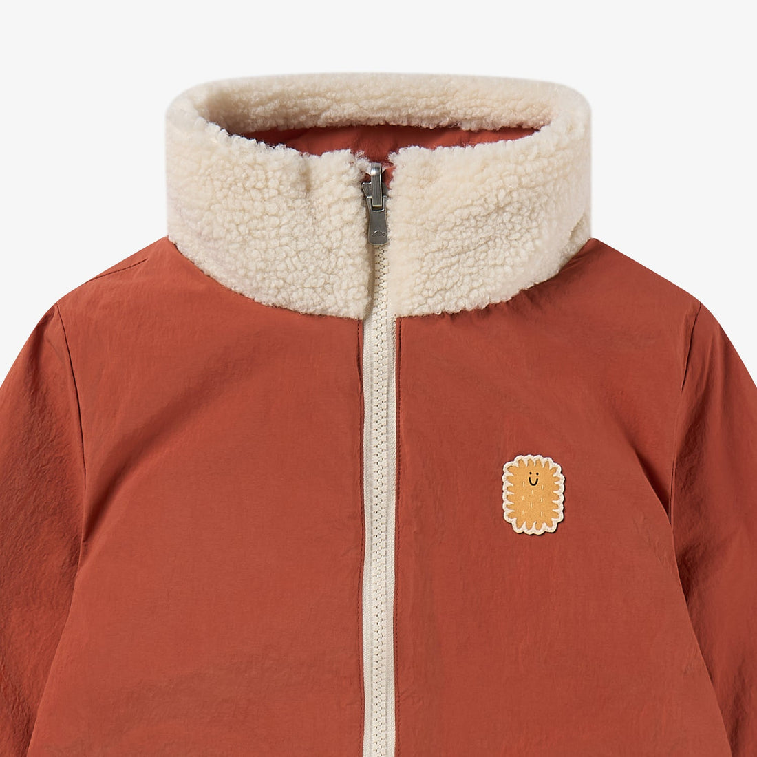 Nest Designs Cozy Crumbs reversible jacket in Redwood Burl rust, upper nylon close-up with fleece collar and smiling biscuit patch