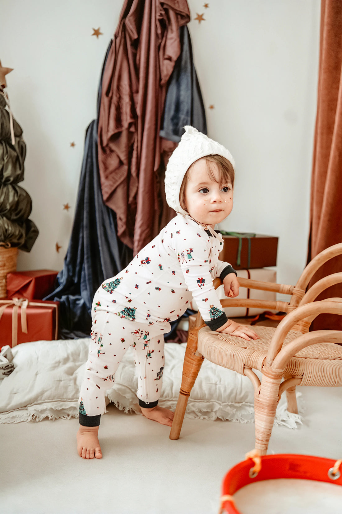 Nest Designs Santas Elves: child standing beside a chair in the footless sleeper; the separate hat is not included