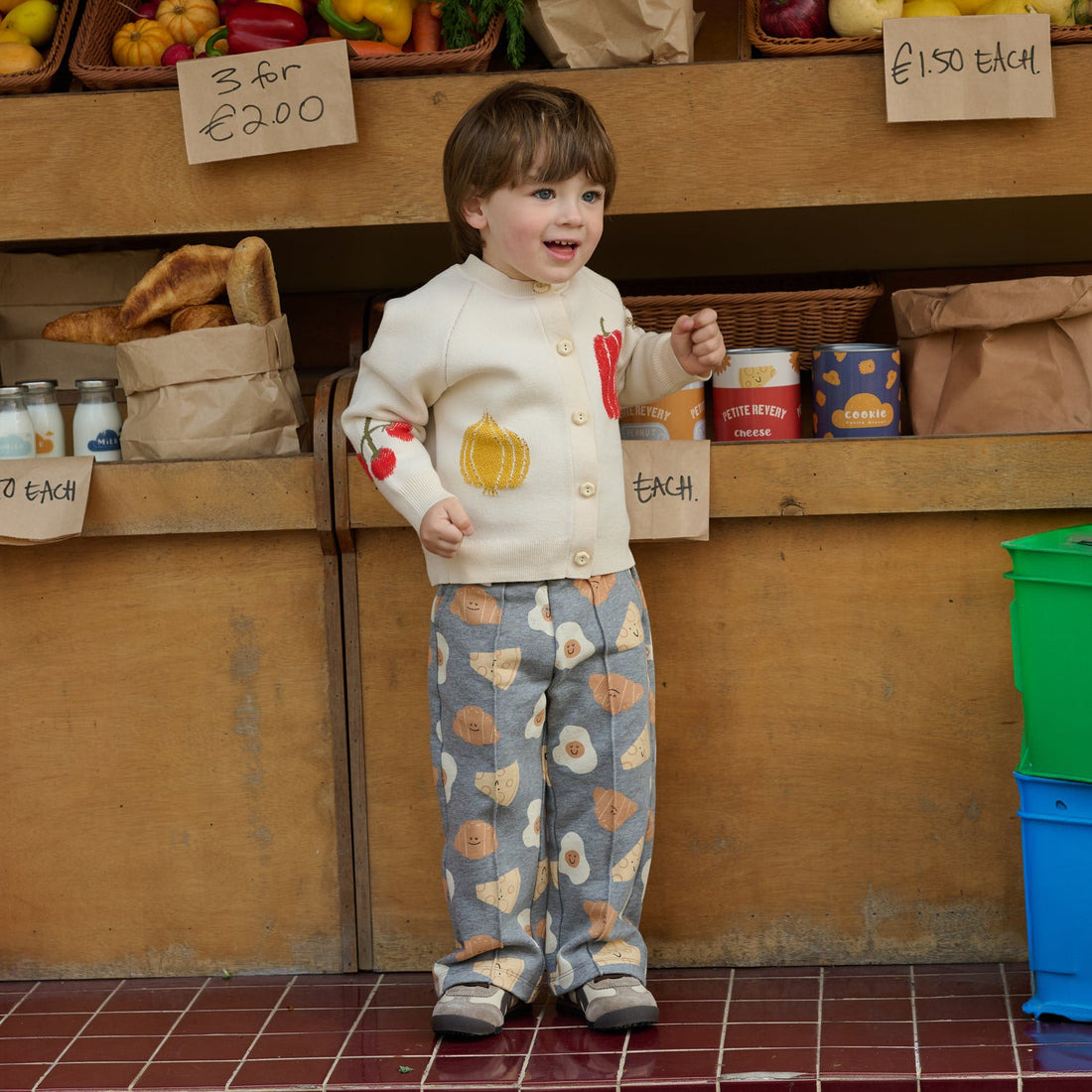 Nest Designs Jet Stream cream knit cardigan worn buttoned by a smiling child with printed trousers at a market
