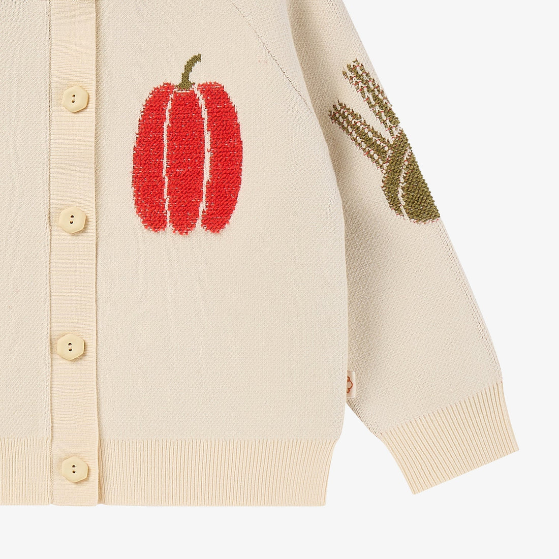 Nest Designs Jet Stream cream knit cardigan, lower detail with red pepper, green sleeve motif, ribbed hem, and cuff