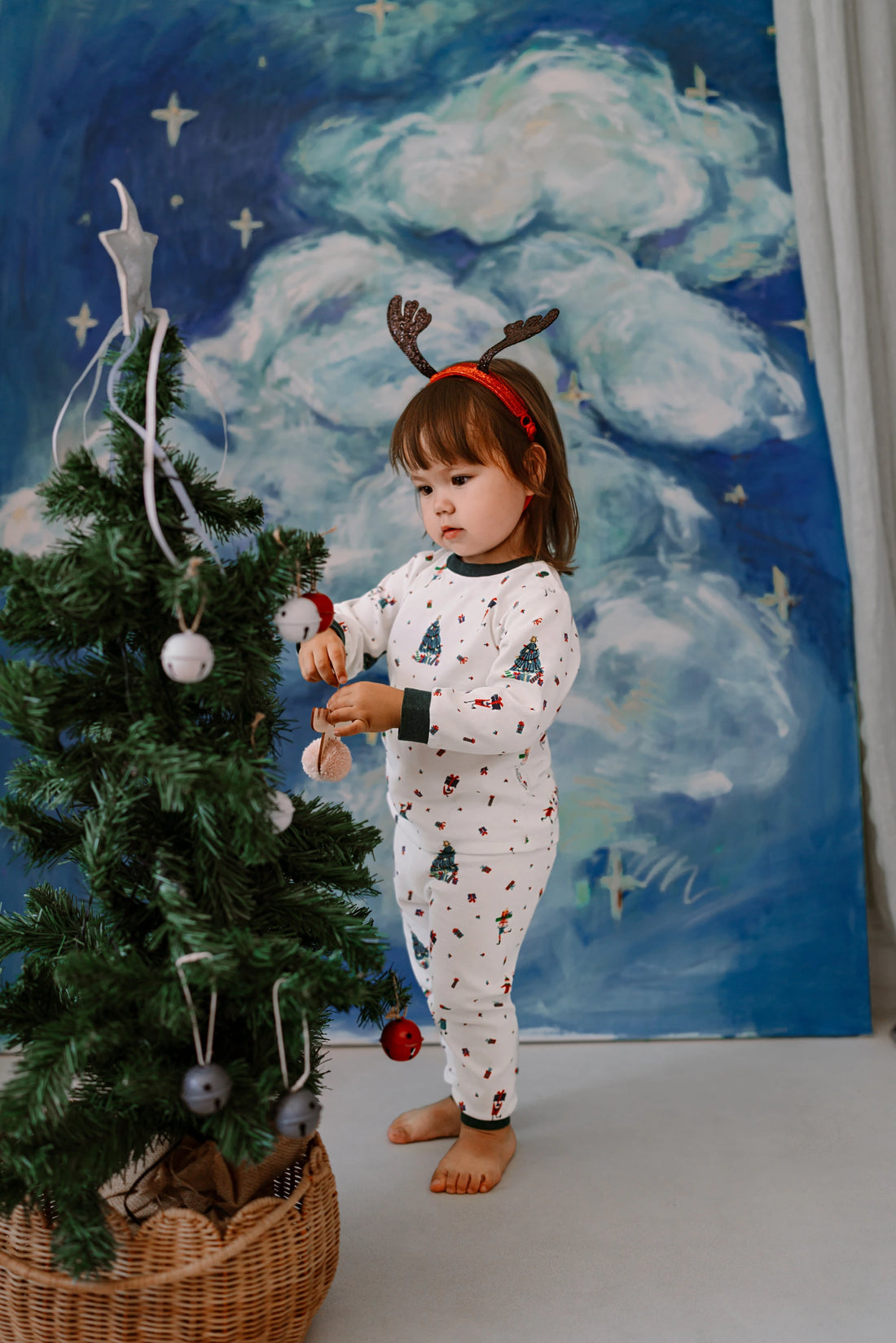Nest Designs Santas Elves: child wearing the matching pajama set beside a holiday tree