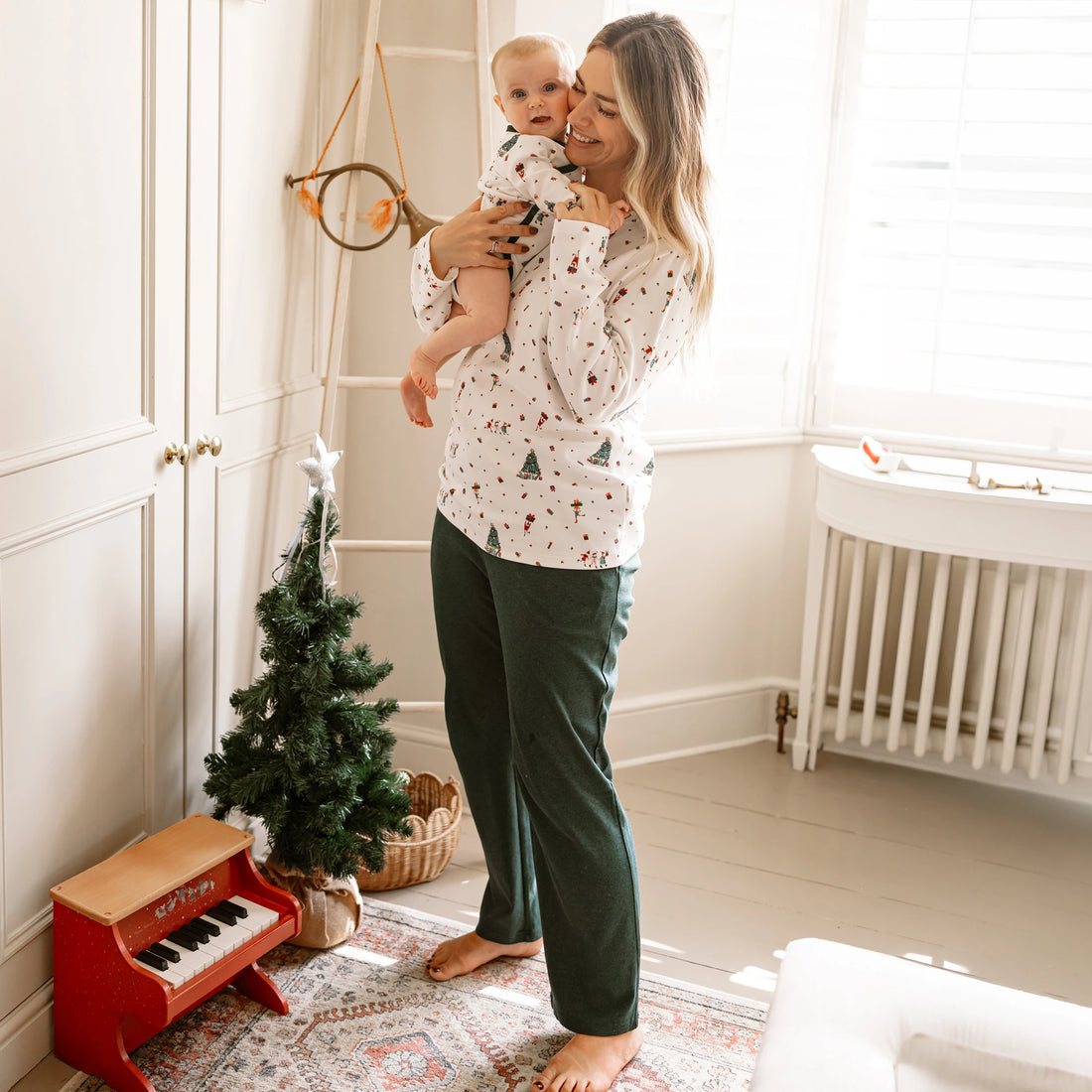 Nest Designs Santas Elves: caregiver standing by a window with a baby wearing the kimono onesie